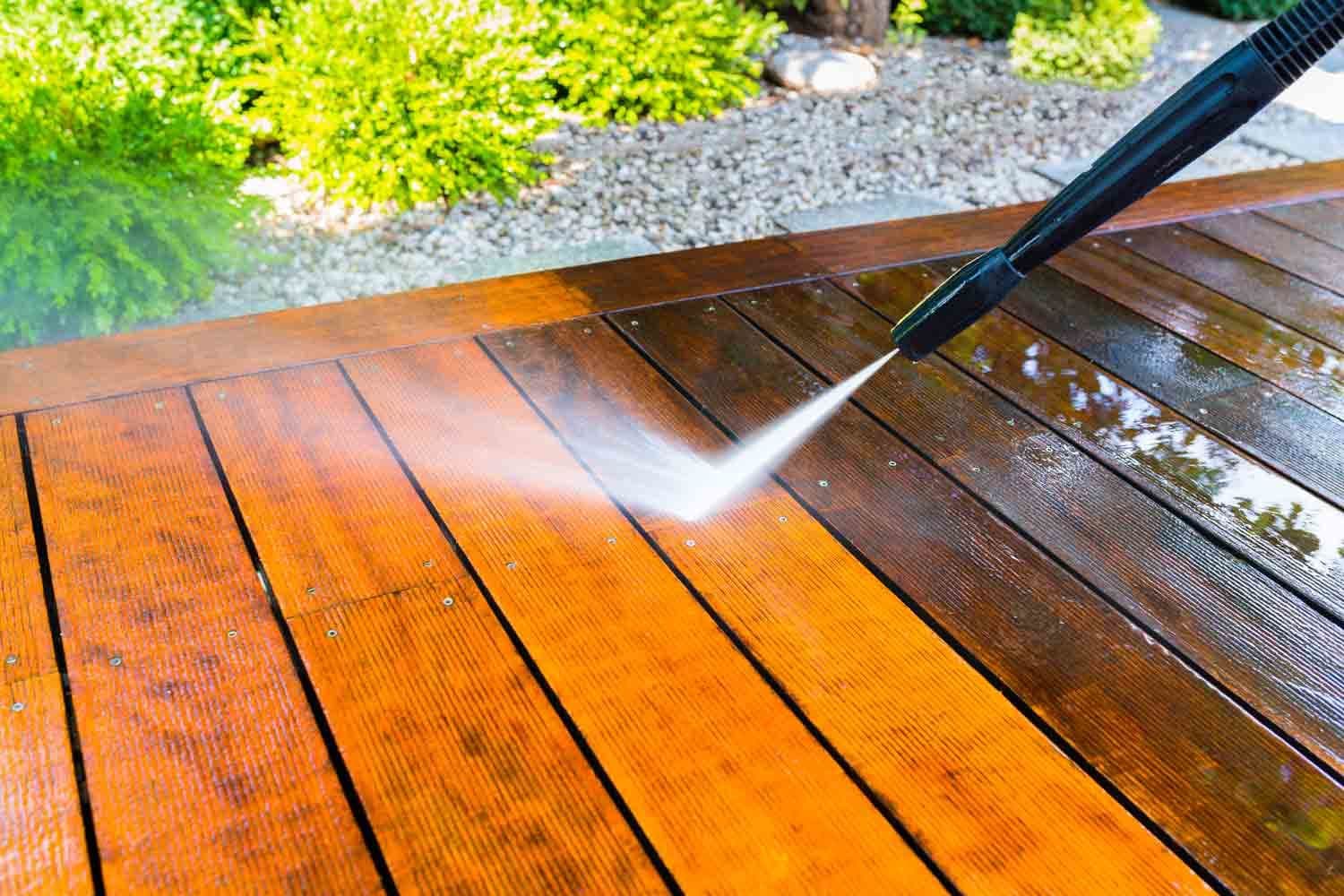 A pressure washer wand stripping grime off a wooden deck, clean boards beside dirty ones