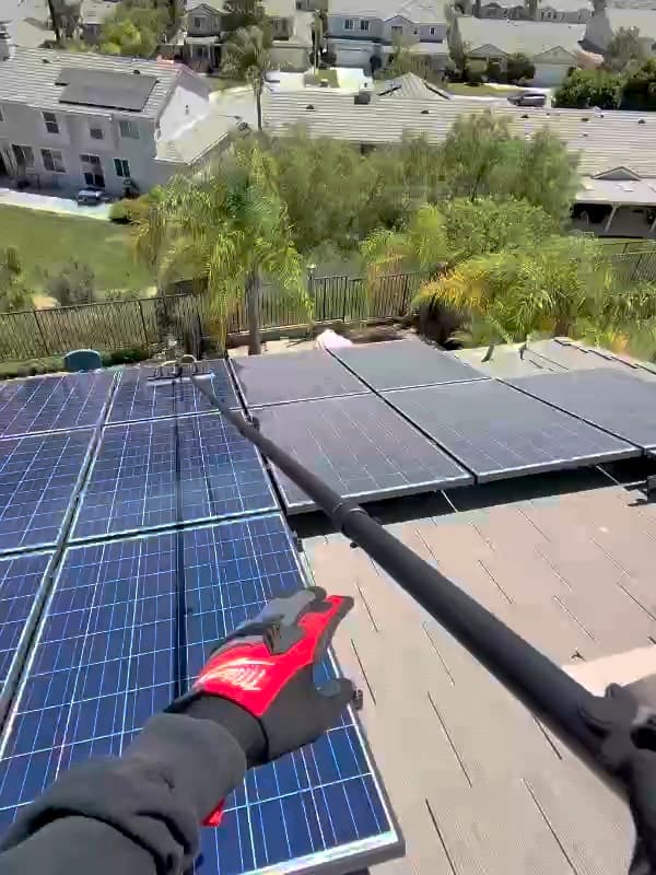 First-person view of an Aurix technician cleaning solar panels with a water-fed soft-bristle brush